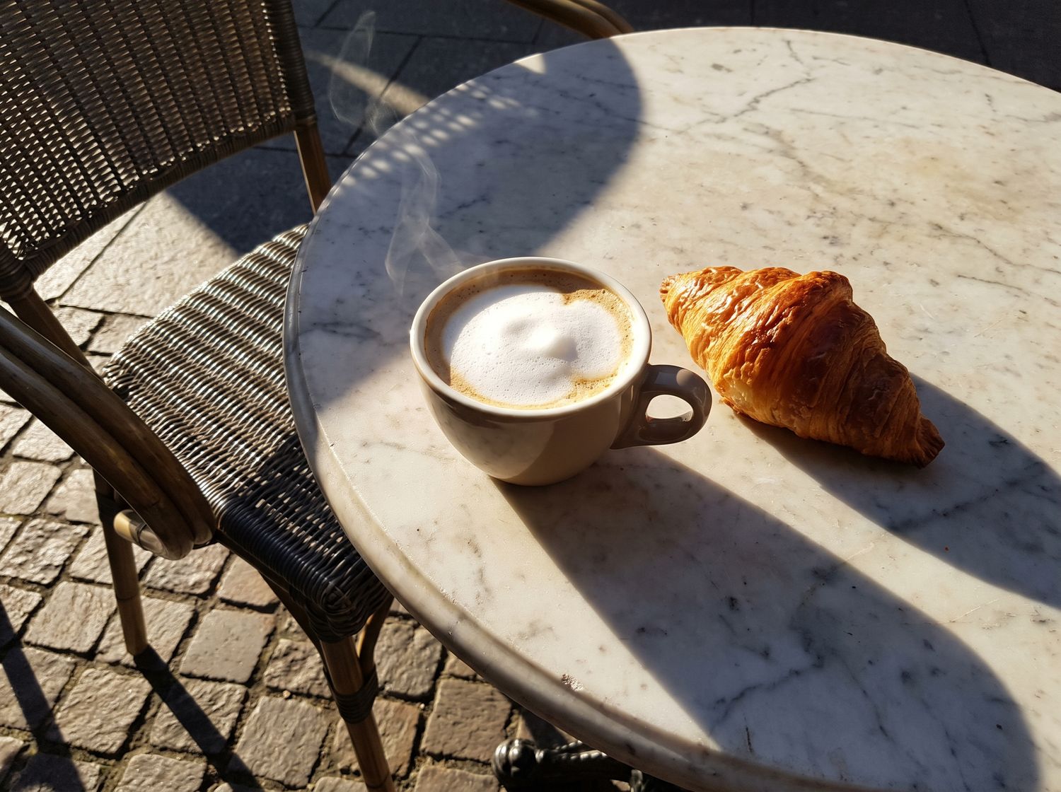 Café crème et croissant sur une petite table en marbre, dans le soleil du matin